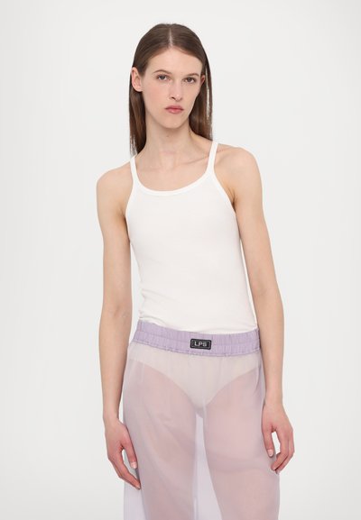 Débardeur en coton blanc à fines bretelles associé à un pantalon lavande transparent avec une taille élastique et une étiquette logo à l'avant.