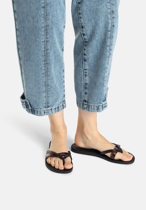 Schwarze Flip-Flops mit einer strukturierten Sohle und einem crisscross-Design, das ein dezentes Schildpatt-Muster aufweist. Getragen mit hochgekrempelten Jeans.