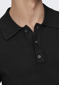 Schwarzes Poloshirt aus strukturiertem Stoff mit einem kragenförmigen Ausschnitt, Knopfschluss und subtilen gerippten Details am Kragen.