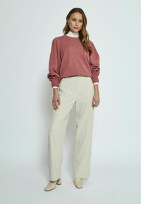 Red knit sweater with wide sleeves, paired with cream wide-leg trousers. The model wears beige block-heeled shoes and a white turtleneck underneath.