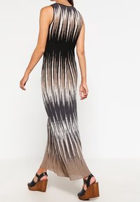 Robe longue sans manches noire et beige avec un motif à rayures verticales. Tissu tricoté avec une coupe fluide et un ourlet qui tombe jusqu'au sol.