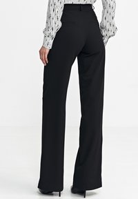 Czarne spodnie o szerokich nogawkach wykonane z gładkiego materiału, z tylnymi kieszeniami i dopasowanym talią. Odpowiednie zarówno na formalne, jak i casualowe okazje.