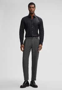 Schwarzes Hemd mit Knöpfen, graue karierte Hose und schwarze Lederschuhe. Slim Fit, glatte Textur, saubere Nähte und klassisches Design.