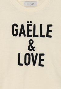 Maglione a maglia color crema con testo ricamato nero che recita "GAËLLE & LOVE." Presenta un collo rotondo e una texture morbida.