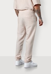 Light pink patterned joggers with an elastic waistband and side pockets, featuring a textured fabric and relaxed fit, paired with white sneakers.