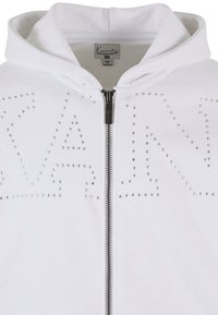 Hvit zip-up hettegenser med sølv nagler som danner bokstavene "KAN" på forsiden, med standard hette og sølv glidelås.