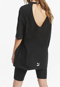 T-shirt nera oversized con schiena aperta, dotata di maniche corte e logo Puma vicino all'orlo. Indossata con leggings neri da ciclismo.