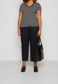 Maglietta a maniche corte a righe bianche e nere con scollo a V, pantaloni blu navy, borsa tote nera e mocassini neri con dettagli dorati.