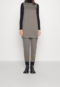 Tunique à carreaux noir et blanc sur un pantalon taille haute assorti, avec des poignets côtes noirs et un col montant. Des bottes à talons noirs complètent l'ensemble.