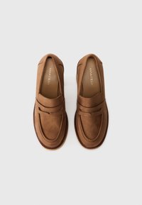 Ruske suede loafers z zaobljenim nosom, šivi in podrobnosti ter dvignjen trak čez zgornji del. Gladka tekstura in raven podplat.