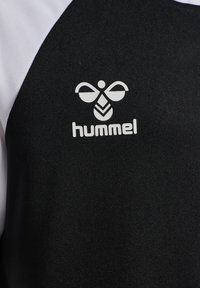 Sort sportstrøje med hvide accenter, der har et tekstureret stof og et logo, der ligner en stiliseret bi.