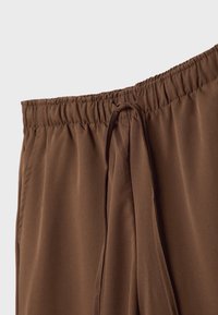 Hnědé kalhoty s elastickým pasem a šňůrkovým zapínáním, vyrobené z lehké látky, s hladkým povrchem a minimalistickým designem.