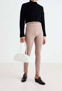 Czarny prążkowany krótki sweter z białym obramowaniem, beżowe dopasowane spodnie z detalami szwów oraz biała torebka. Czarne buty na niskim obcasie.