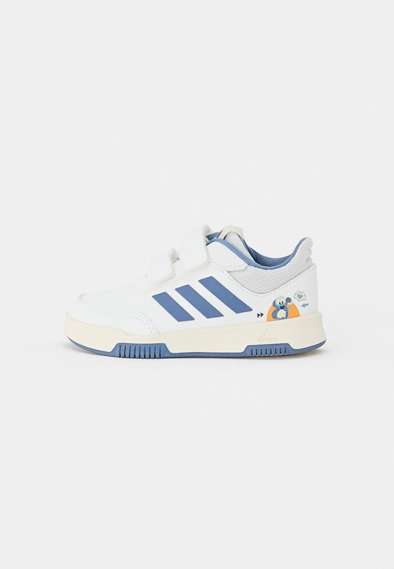 Fehér sportcipők kék díszítéssel, három kék csíkkal, tépőzárral és mesefigurás mintával a külső oldalon.