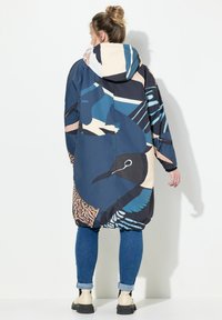 Cappotto capuccio colorato con un motivo di uccelli in tonalità di blu, beige e nero. Maniche lunghe e vestibilità rilassata, realizzato in un materiale leggero.