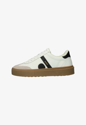 White sneaker with black and tan accents, leather upper, rounded toe, flat gum sole, lace-up design, and a soft lining.