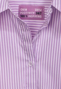 Light purple button-up shirt with white vertical stripes, pointed collar, and a tag that reads "Pure Positivity 24/7, 100% Inspiring."