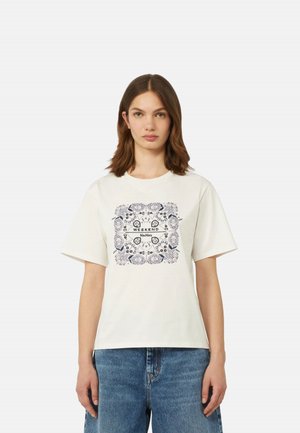 Giovane donna che indossa una maglietta bianca a maniche corte con stampa bandana floreale blu navy e scritta "Weekend MaxMara", abbinata a jeans in denim blu.