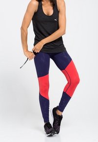 Svart linne, marinblå och röda leggings med färgblockering och texturerade paneler, i kombination med svarta sportskor. Texturerade tyger.