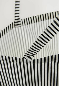 Borsa a spalla in tessuto a righe bianche e nere con due tracolle verticali, caratterizzata da una forma rettangolare e una morbida texture tessile.