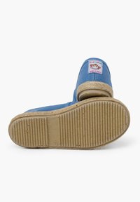Scarpe di tela blu con suola in morbida paglia, caratterizzate da un patch con un design di scimmia. Il design include dettagli testurizzati e una forma arrotondata.