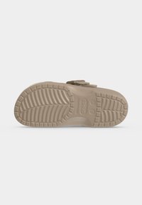 Σόλα από μπεζ κλογκ Crocs που δείχνει υφής μοτίβο πέλματος και ανάγλυφο όνομα εμπορικού σήματος σε απλό λευκό φόντο.