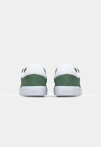 Green suede low-top sneakers with white rubber soles and accents. Lacoste logo on the heel, round toe design. Simple and clean aesthetic.