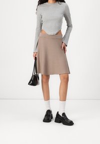 Maglietta grigia a maniche lunghe con taglio cropped, abbinata a una gonna A-line beige lunga fino al ginocchio. Una borsa nera e scarpe nere chunky completano il look.