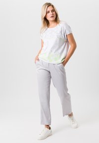 Lichtgrijze t-shirt met korte mouwen en cirkelvormige patronen en tekst, gecombineerd met lichtgrijze, taps toelopende pants en witte sneakers.