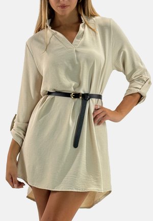 Robe-chemise beige clair avec encolure en V, manches retroussées, et ceinture noire. Texture lisse, longueur au genou avec un ourlet légèrement arrondi.