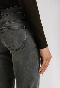 Jeans i denim med en mörkgrå tvätt och en figursydd design, med bakfickor och subtila blekningar. Slät textur och minimalistiska detaljer.