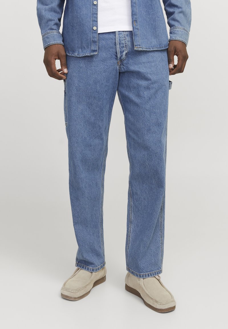 Pantalones cargo de mezclilla azul claro con un corte holgado, piernas rectas, bolsillo lateral y un diseño clásico de 5 bolsillos. Combinados con zapatos de lona beige.