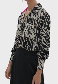 Long-sleeve shirt with a black and beige zebra pattern, featuring a pink collar, button front, and two chest pockets. Soft fabric, relaxed fit.