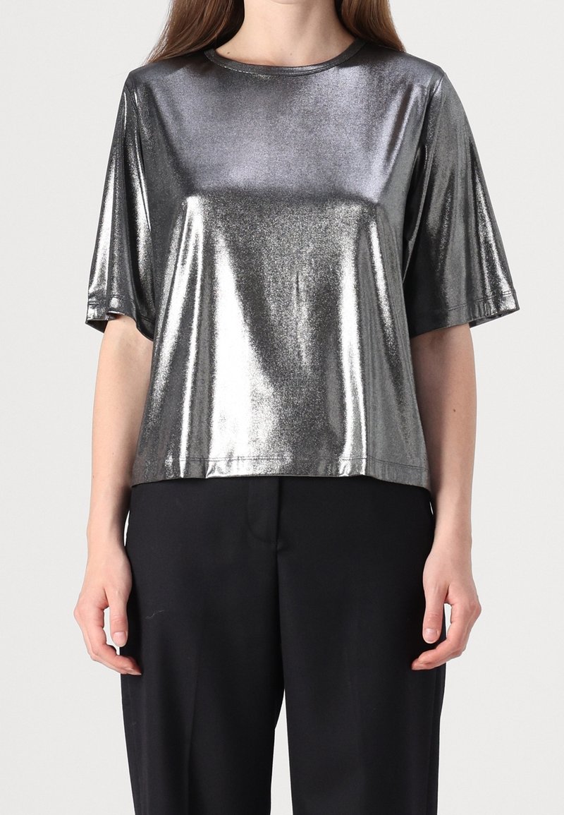 Top corto manica corta in argento metallico con scollatura rotonda e vestibilità rilassata. Il tessuto ha una finitura lucida, in contrasto con pantaloni neri.