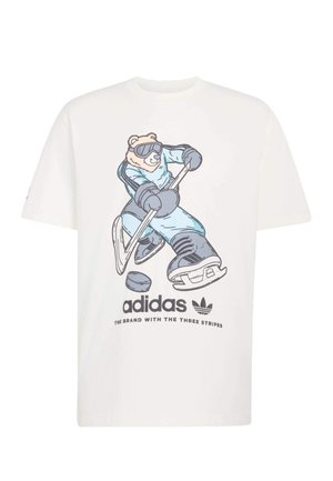 T-shirt en coton blanc avec un motif représentant un ours en tenue de hockey bleue, tenant une crosse, avec le logo Adidas et le slogan imprimés en dessous.