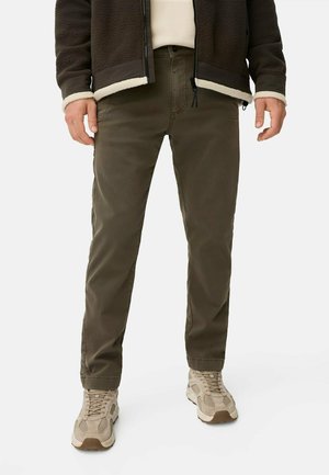 Olive green cotton trousers with a slim fit, featuring front pockets and a zip fly, paired with beige athletic shoes.