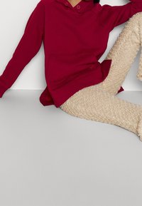 Sudadera con capucha color marrón burdeos con un bolsillo tipo canguro, combinada con pantalones de punto beige y esponjosos con puños acanalados. Ambas prendas tienen un corte holgado.