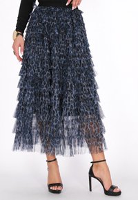 Két rétegű tüll szoknya kék és fekete leopárdmintával, réteges fodrokkal és áttetsző textúrával, fekete pántos magassarkú cipővel párosítva.