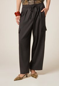 Pantalones de pierna ancha grises con cintura ajustable, que cuentan con bolsillos laterales. Combinados con tacones con estampado y pulseras de madera.