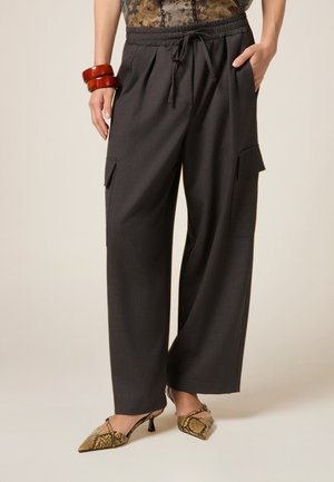 Pantaloni a gamba larga grigi con vita regolabile, dotati di tasche laterali. Indossati con tacchi a fantasia e braccialetti in legno.