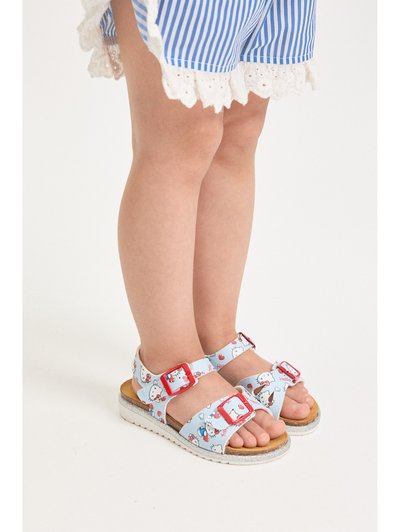 Παιδί που φοράει μπλε και λευκά ριγέ σορτς και ανοιχτό μπλε σανδάλια με κόκκινες αγκράφες και σχέδιο με χαρακτήρα κινουμένων σχεδίων, που στέκεται σε λευκό πάτωμα.