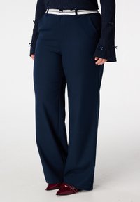 Marineblauwe wijde broek met een gladde textuur, voorzien van een witte riem en zijzakken. Gecombineerd met puntige bordeauxrode hakken.