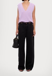 Top senza maniche in maglia lavanda con scollo a V, abbinato a jeans neri a vita alta e a gamba larga. La borsa nera e i sandali open-toe completano il look.