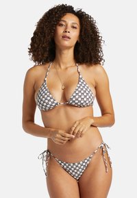 Bikini set s trojuholníkovými vrchnými časťami a viazanými spodkami v čierno-bielom geometrickom vzore, vyrobený z elastického materiálu s lesklými akcentmi.
