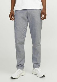 Pantalones ligeros grises con una textura sutil, piernas ajustadas, bolsillos laterales, usados con zapatillas deportivas blancas.