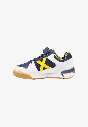 Zapatilla de bajo perfil para niños con cuero blanco, malla azul marino, detalle amarillo en forma de "X", cordones y tira azul marino, y suela de goma marrón claro.