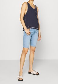 Marineblauw tanktop met een borstzak, gecombineerd met lichtblauwe denim shorts en lichtroze sandalen met een gespdetail.