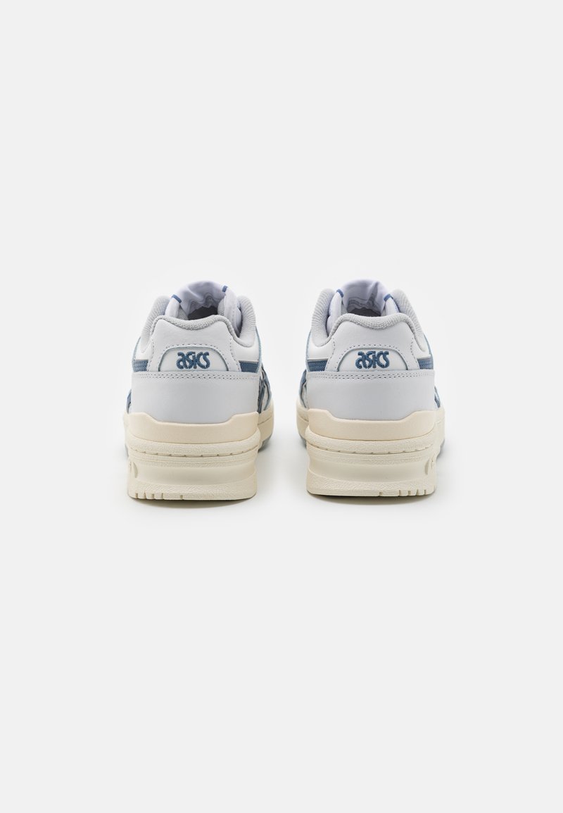 Baskets en cuir blanc avec des accents bleus, col rembourré, semelle en caoutchouc et finition texturée, présentant un logo au niveau du talon et sur le côté.