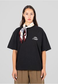 Czarny bawełniany t-shirt z krótkim rękawem, z białym logo na lewym piersi. Na szyi związana jedwabna chusta o wzorze.