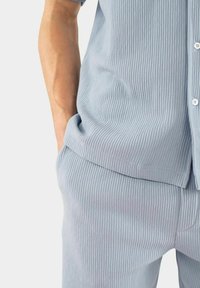 Ljusblå ribbad tvådelad outfit bestående av en kortärmad skjorta med knappar och löst sittande byxor med fickor. Mjuk textur genom hela.